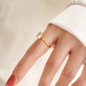 Close-up of elegant gold plated ring with oval zircon on model wearing white blazer