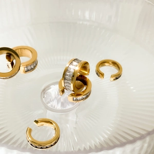 Ear cuff in acciaio placcato oro con zirconi su un vassoio di vetro rigato