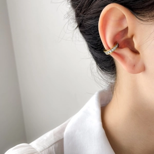 Dettaglio di un ear cuff in titanio placcato oro con zirconi scintillanti sull'orecchio
