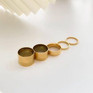 Detail of five stackable wide polished gold minimalist metal rings on beige background