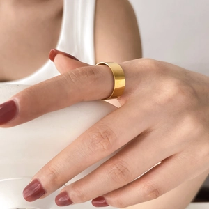 Polished wide gold band ring worn on index finger with a minimalist modern aesthetic