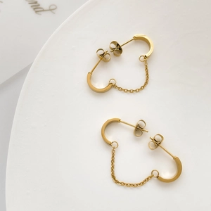 Detail view of gold U-shaped earrings with chain connection on a white ceramic plate