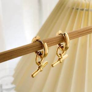 Close-up of golden geometric U-shaped earrings with OT toggle pendant on a wooden stand