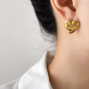 Close-up of heart-shaped gold earring with crystal pavé on a model's ear
