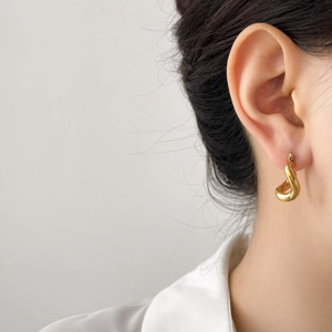 Minimalist gold-plated drop earring on a model's ear with high-gloss metallic finish