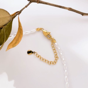 Détail de collier en perles blanches montrant le fermoir mousqueton doré et la chaînette