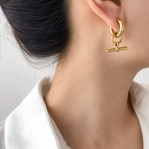 Close-up of minimalist gold T-bar pendant earring on model for modern fashion look