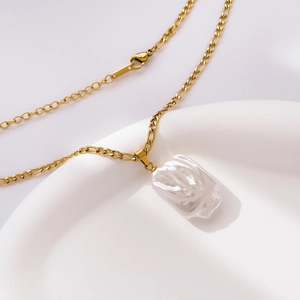 Vue détaillée d'un collier en perle baroque dorée sur le bord d'un plat en céramique