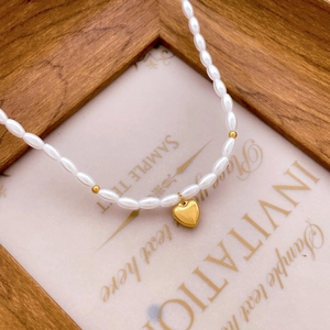 Gros plan sur un collier de perles ovales avec un pendentif cœur doré poli élégant