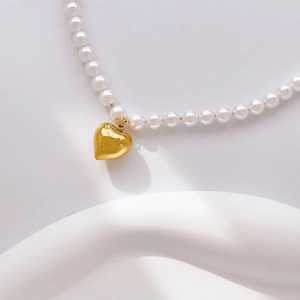 Détail d'un collier de perles blanches avec pendentif coeur doré sur support blanc