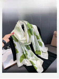 Detail of silk-feel scarf with green ginkgo leaf pattern on white fabric texture
