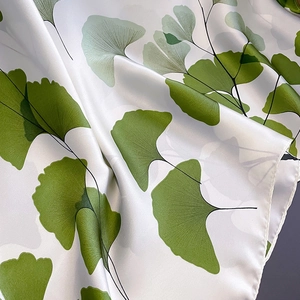 Detail of silk scarf showing green ginkgo leaf print and refined rolled edge texture