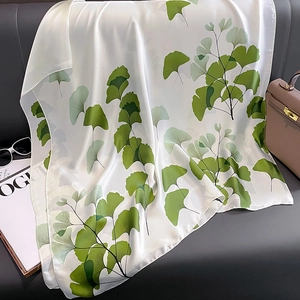 Elegant ivory silk scarf with green ginkgo leaf print draped on a grey sofa background