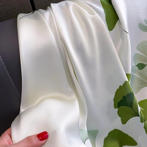 Close-up of silk scarf fabric featuring green ginkgo leaves on ivory background