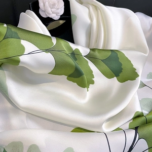 Luxurious ivory silk scarf with vibrant green ginkgo leaves pattern and soft drape
