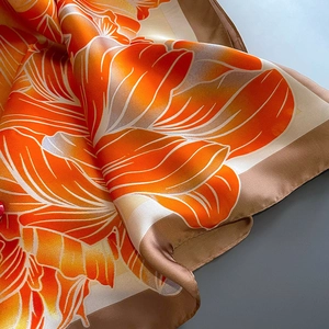 Détail d'un foulard en soie avec imprimés floraux orange et finition satinée
