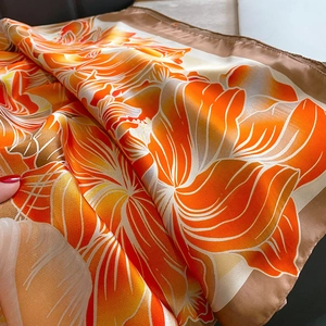 Détail d'un imprimé floral orange sur une écharpe en satin soyeux avec bords ourlés