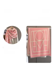 Detail of pink knit shawl scarf with H and M geometric letter patterns on a white coat