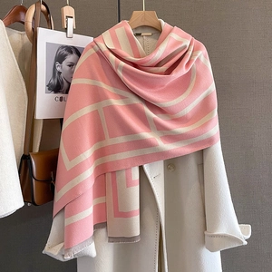 Pink and beige geometric knit scarf with fringe styled on a white coat for winter warmth