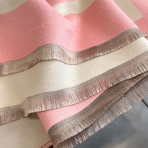 Detailed view of pink and beige striped knit scarf with golden fringe tassels