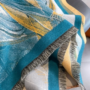 Detail of jacquard knit scarf showing teal and yellow abstract texture with fine tassels