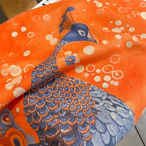 Detailed macro shot of orange cashmere-feel scarf fabric featuring blue peacock patterns