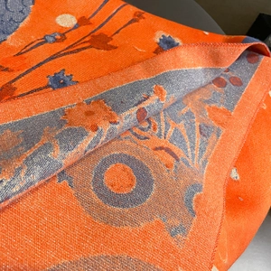 Detail of orange and blue floral knit scarf with gold glitter thread and jacquard texture