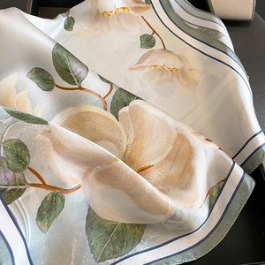 Elegant silk scarf with magnolia print and green striped border on dark background