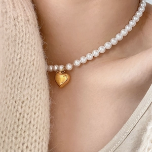 Gros plan d'un collier de perles avec pendentif cœur doré poli porté par un mannequin