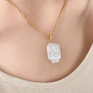 Gros plan d'un collier chaîne Figaro dorée avec un pendentif perle baroque sur un mannequin