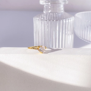Dettaglio di un anello dorato con zircone a cuore su un supporto geometrico bianco