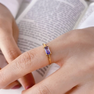 Dettaglio di un anello minimalista dorato con zircone viola rettangolare sulla mano
