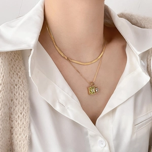 Mehrlagige goldene Schlangenkette mit Zirkon- und Muschel-Anhängern auf weißem Hemd