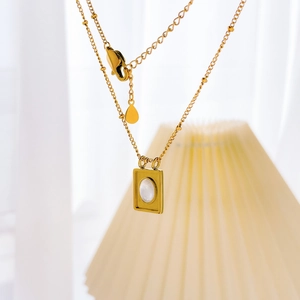Détail d'un collier en titane plaqué or avec pendentif rectangulaire en nacre et chaîne