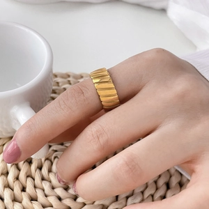 Close-up of a gold wavy textured ring on a finger with a cozy lifestyle background