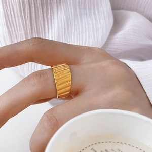 Macro detail of wide gold ring with wavy vertical ridges on textured fabric