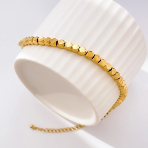 Close-up of gold fish scale chain bracelet with geometric beads on ceramic base