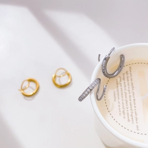 Detailed view of gold hoop earrings and silver pave-set zircon earrings on a candle