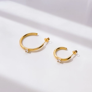 Macro shot of gold C-shape stud earrings with zircon inlay and butterfly backings