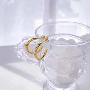 Elegant gold C-shaped zircon hoop earrings displayed on a glass with ice cubes