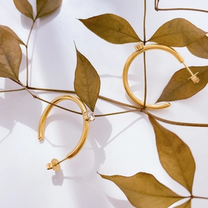 Macro detail of gold C-shape hoop earrings with micro zircon stone on nature branch