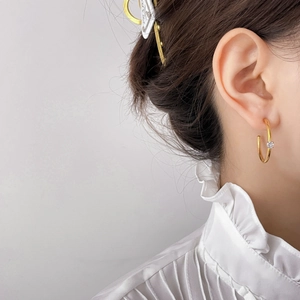 Close-up of a minimalist gold hoop earring with a single zircon stud on a female model