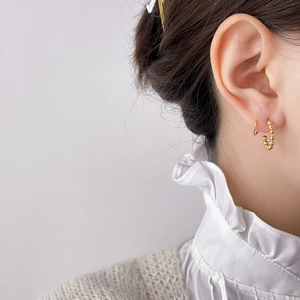 Close-up of gold C-shaped beaded earrings with zircon inlay worn by a model