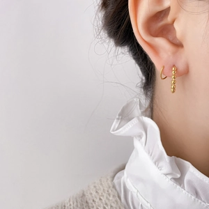 Close-up of gold beaded C-shape earrings and zircon stud set worn on ear