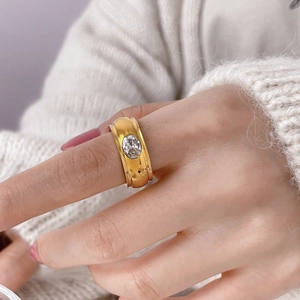 Detail of a wide gold ring with an oval clear zircon set on a polished metallic band
