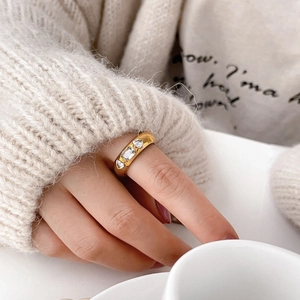 Close-up of a wide gold band ring with three zircons worn by a model holding a cup