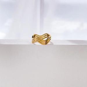 Vue détaillée d'une bague dorée ondulée à trois couches sur support en pierre blanche