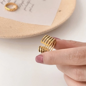 Macro d'une bague ouverte dorée à couches géométriques ajourées montrant sa finition métallique