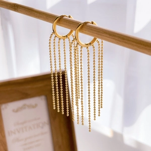 Detailed close-up of gold tassel drop earrings with beaded chains on a wooden hanger
