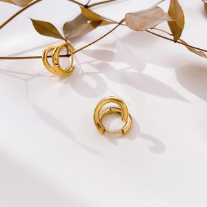 Detail of gold double-layered hoop earrings with textured finish on a minimalist background